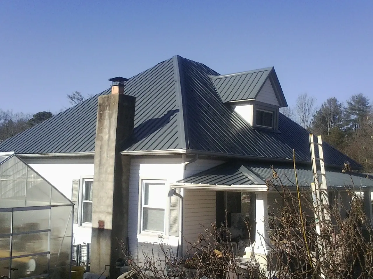 Dark blue standing seam metal roof on a white farmhouse with dormer — Slate & Tile Roof Repair by Roofing Brothers in West Bloomfield