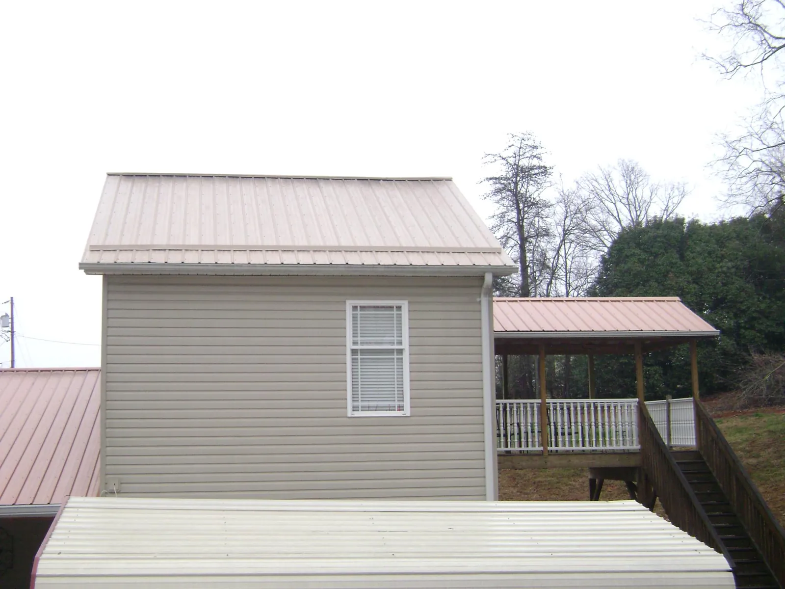 Tan metal roofs on a two story addition and attached porch, from a Roof Replacement job in West Bloomfield